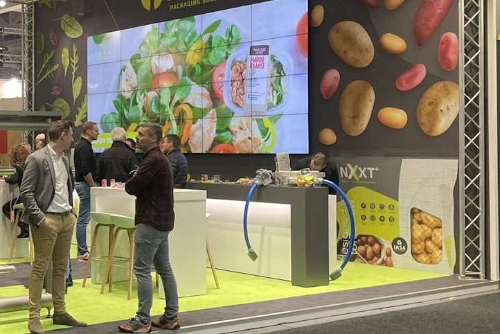 Modulaire beursstand met 5 meter hoge systeemkaders. De modulaire beurswand is met full colour peesdoek afgewerkt. Om de videowall te bevestigen hebben we onze modulaire houten tussenplaten gemonteerd.